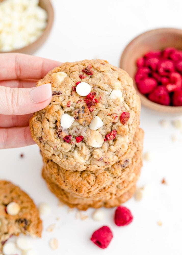 picture of a cookie being held up by the camera with a stack of cookies and bowl of raspberries in the background 