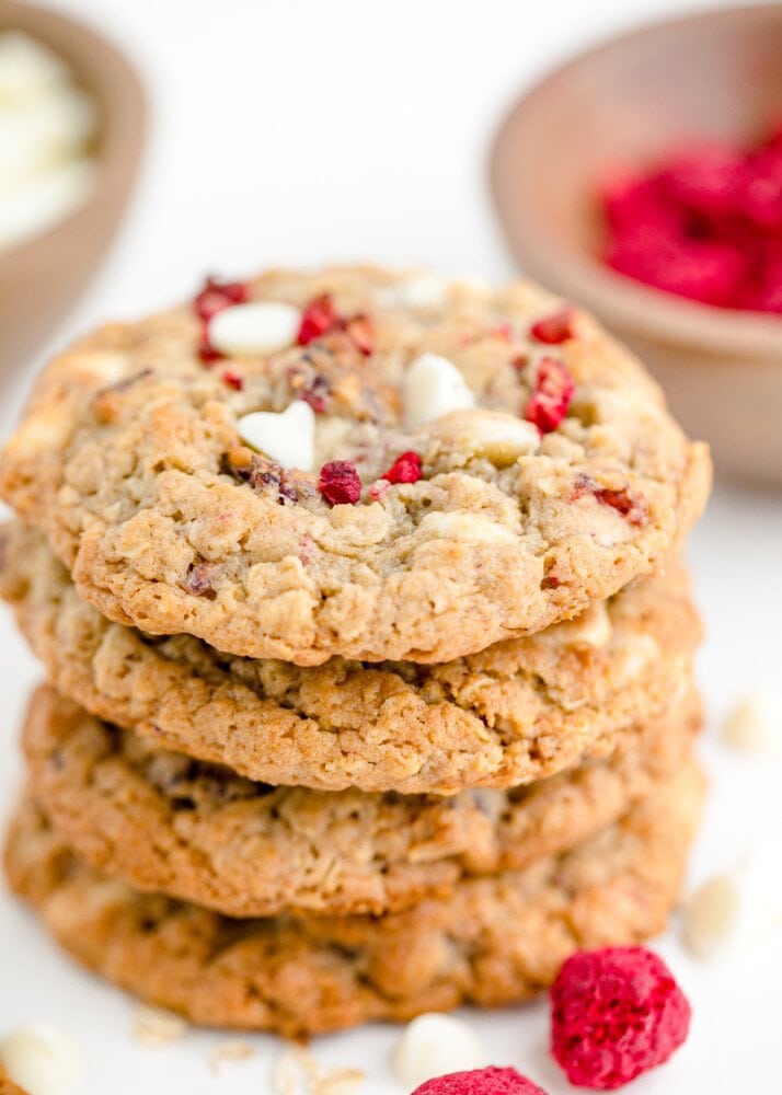 stack of cookies with a bowl of raspberries in the back 