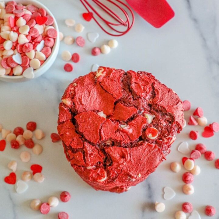picture of red velvet cookie on a white plate surrounded by white and red baking chips