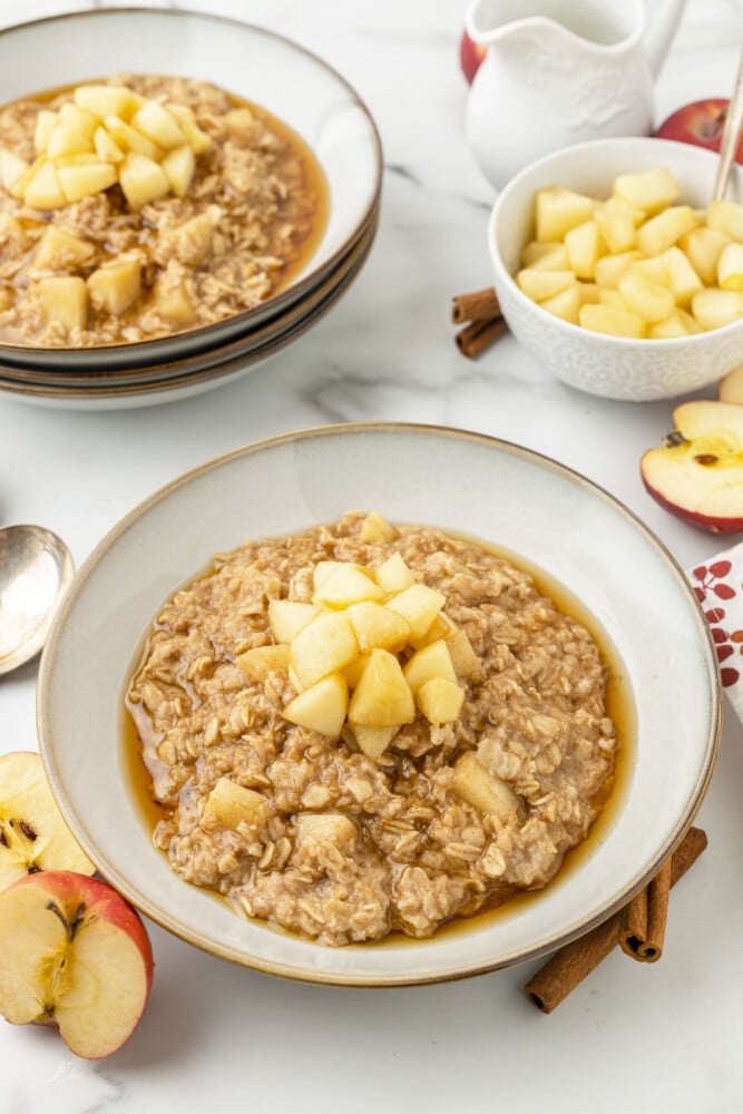 a bowl of oatmeal with apples on top and apples and more oatmeal in the background