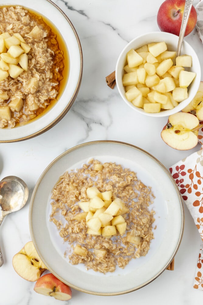 overshot picture of two bowl of oatmeal with apples and a bowl of apples on the right 