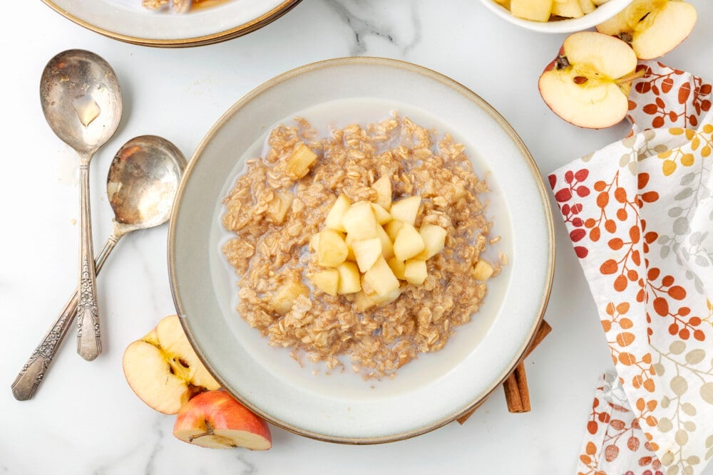 apple cinnamon oatmeal in a bowl with spoons and apples around the bowl 