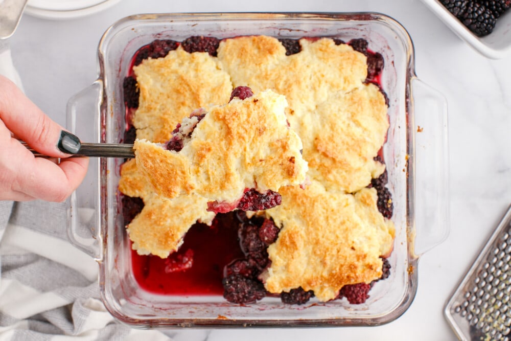 blackberries and crusty topping in a glass dish with a fork in it