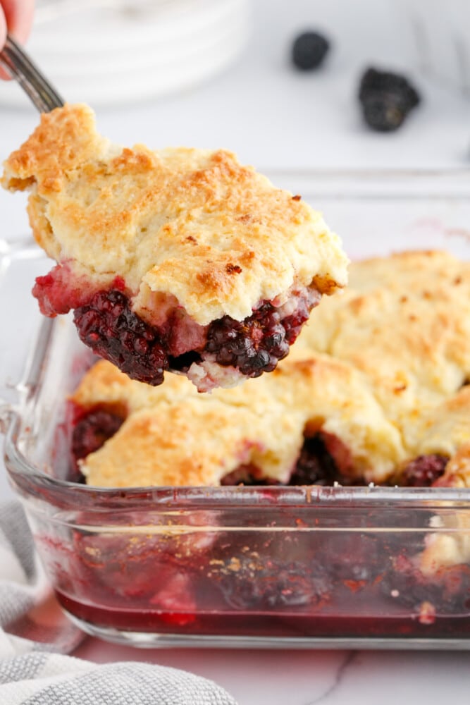 blackberries and crusty topping in a glass dish with a fork in it