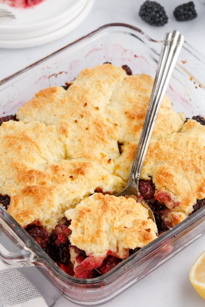 blackberries and crusty topping in a glass dish with a fork in it