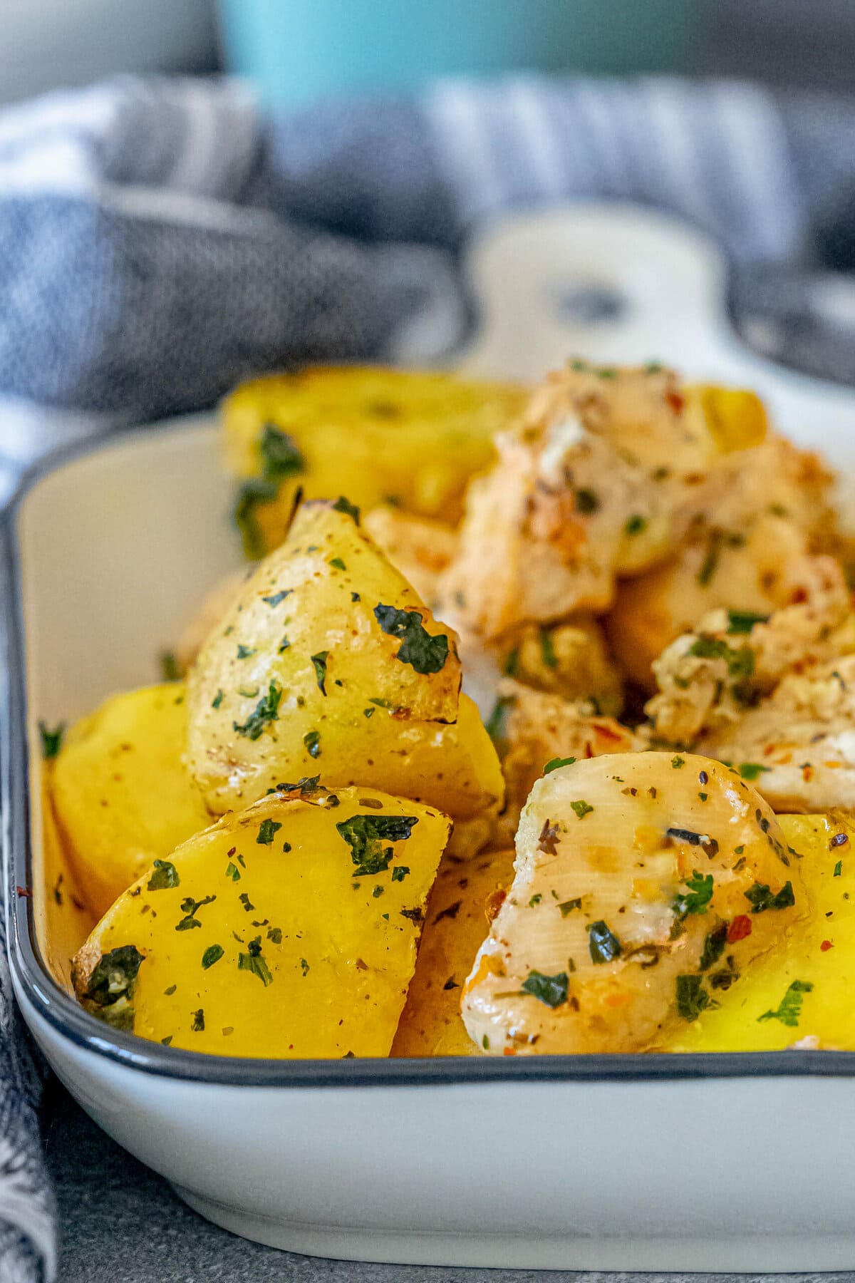 Baked chicken and potatoes with herbs in a white dish.