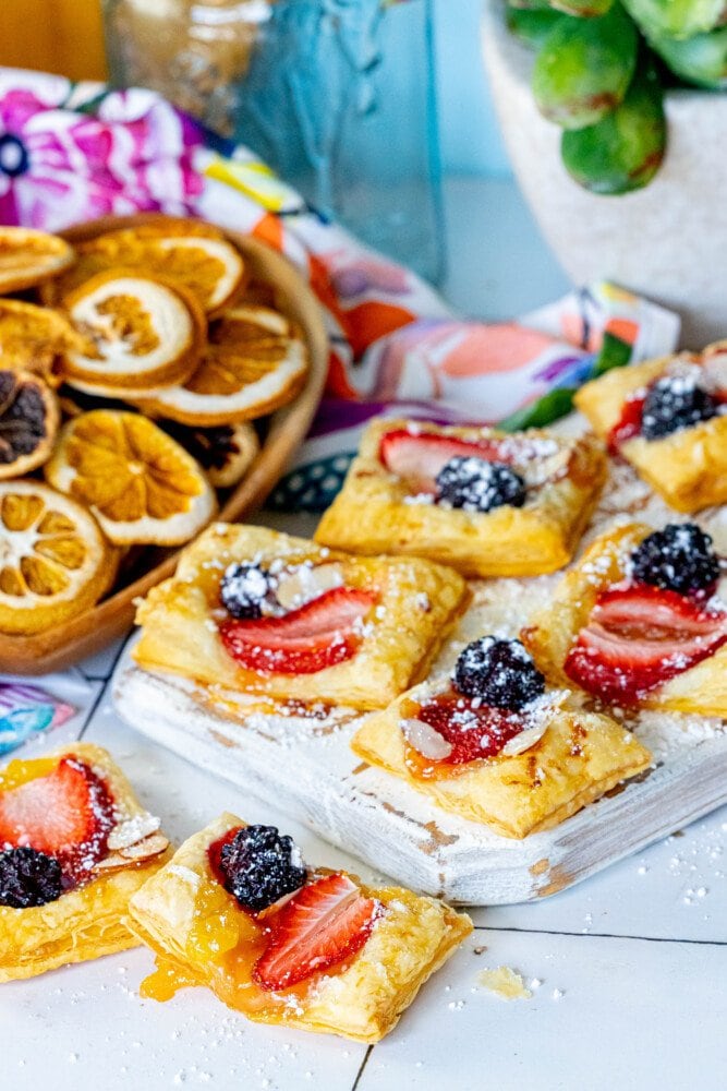 picture of lemon tart with a strawberry, blackberry, and almonds on top on a white cutting board