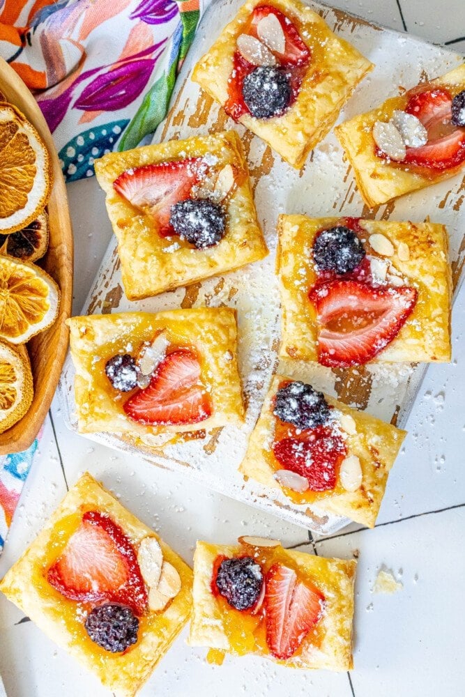 picture of lemon tart with a strawberry, blackberry, and almonds on top on a white cutting board