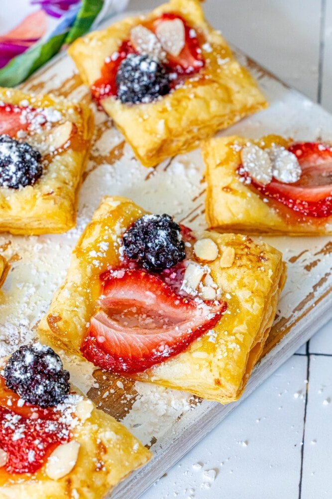 picture of lemon tart with a strawberry, blackberry, and almonds on top on a white cutting board