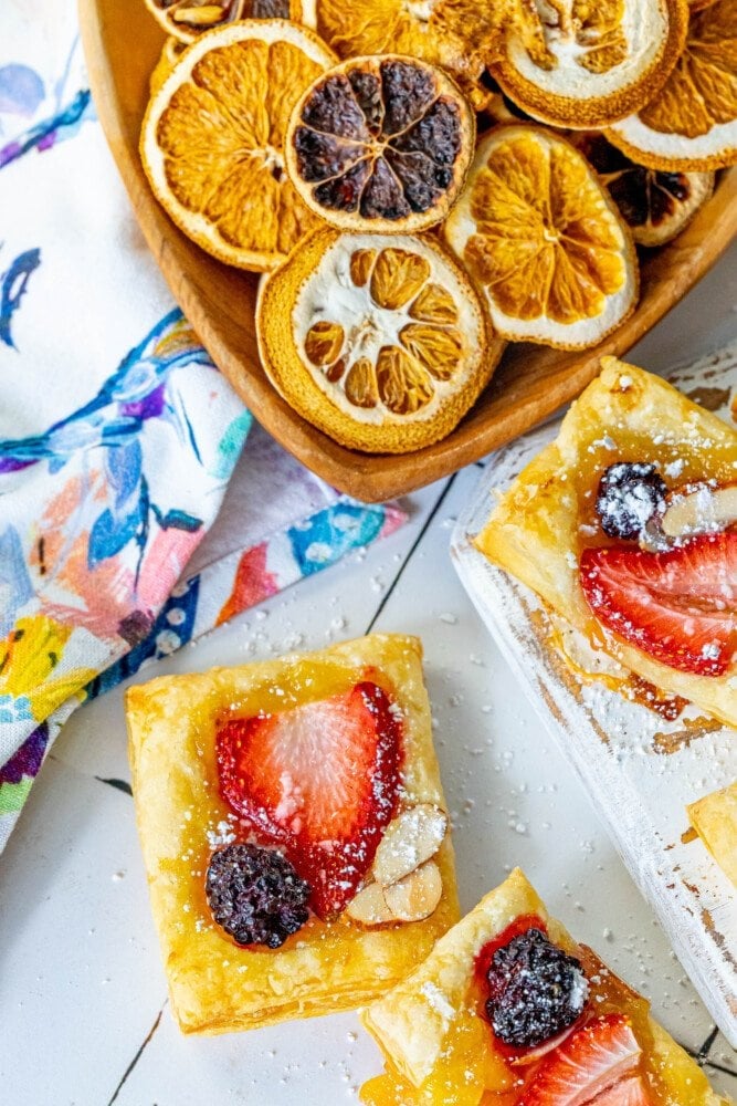 picture of lemon tart with a strawberry, blackberry, and almonds on top on a white cutting board