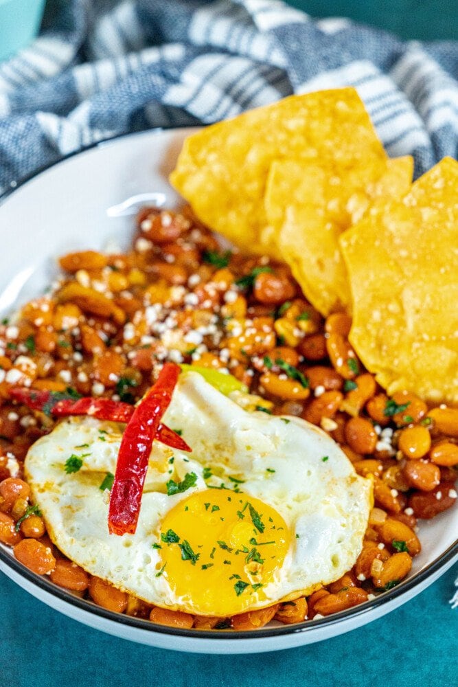 picture of huevos rancheros in a bowl on a table with a fried egg on top and chips in the bowl