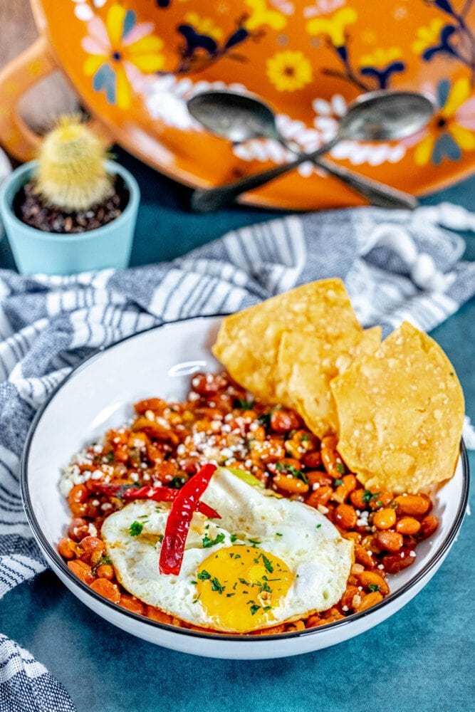 picture of huevos rancheros in a bowl on a table with a fried egg on top and chips in the bowl