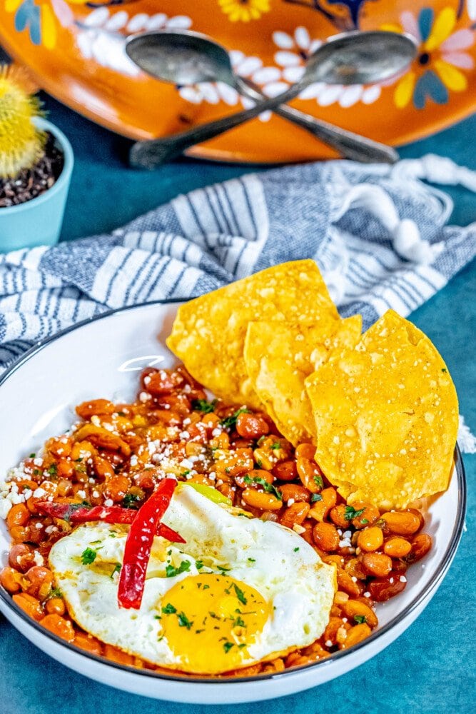 picture of huevos rancheros in a bowl on a table with a fried egg on top and chips in the bowl 