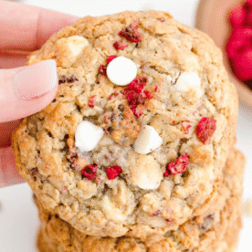 A hand holds an oatmeal cookie studded with white chocolate chips and dried raspberries, highlighting the irresistible combination found in oatmeal cookies white chocolate raspberry.