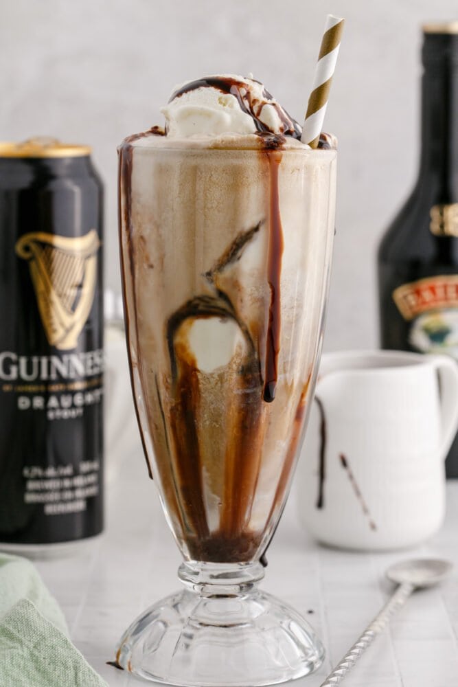 Guinness float in a a glass with a gold paper straw in it and chocolate syrup in the glass