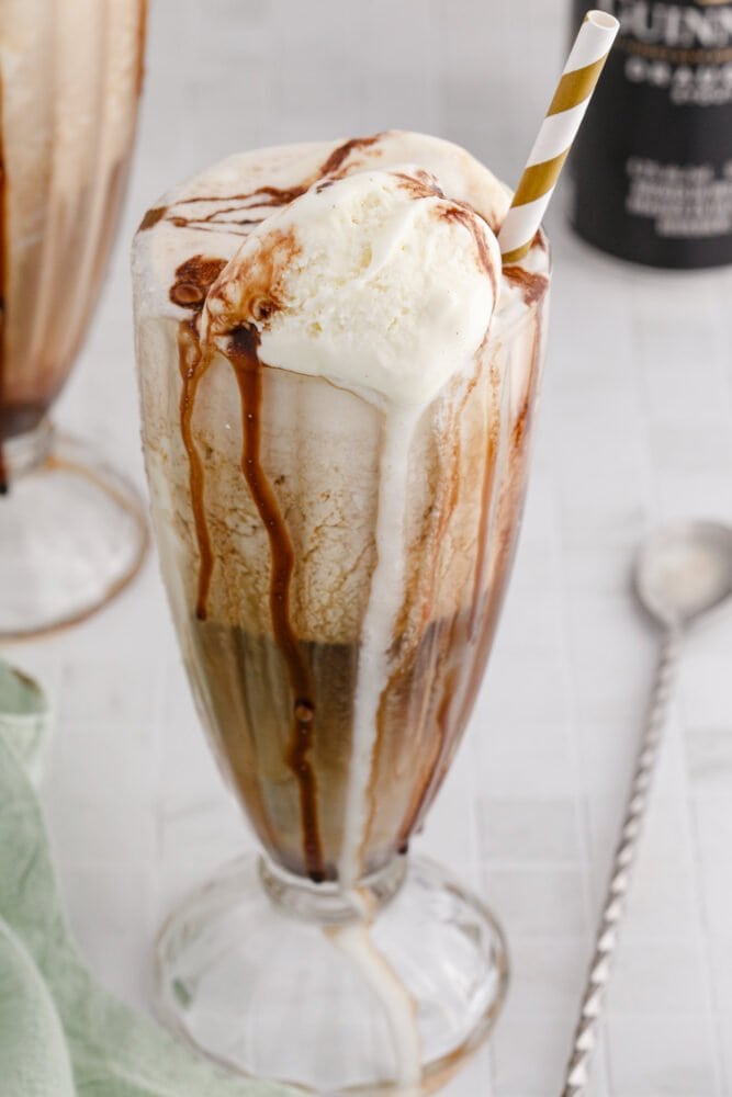 guinness float in a a glass with a gold paper straw in it and chocolate syrup in the glass