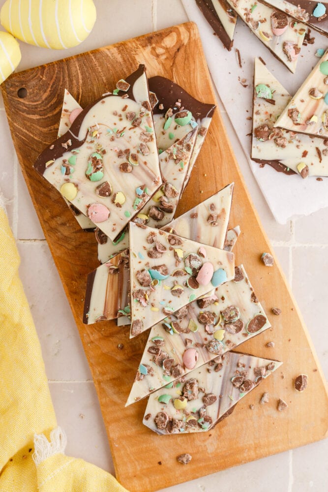 white and dark chocolate bark with m&ms in it on a wooden cutting board