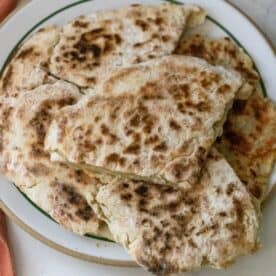 A plate of homemade, golden-brown skillet potato breads stacked on top of each other.