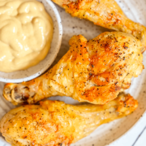 picture of air fried chicken drumsticks on a white plate with mustard dipping sauce next to it