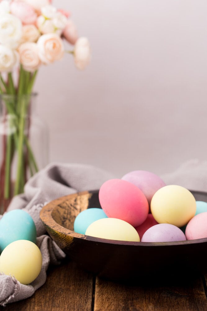 a bowl of Easter eggs with flowers in the back