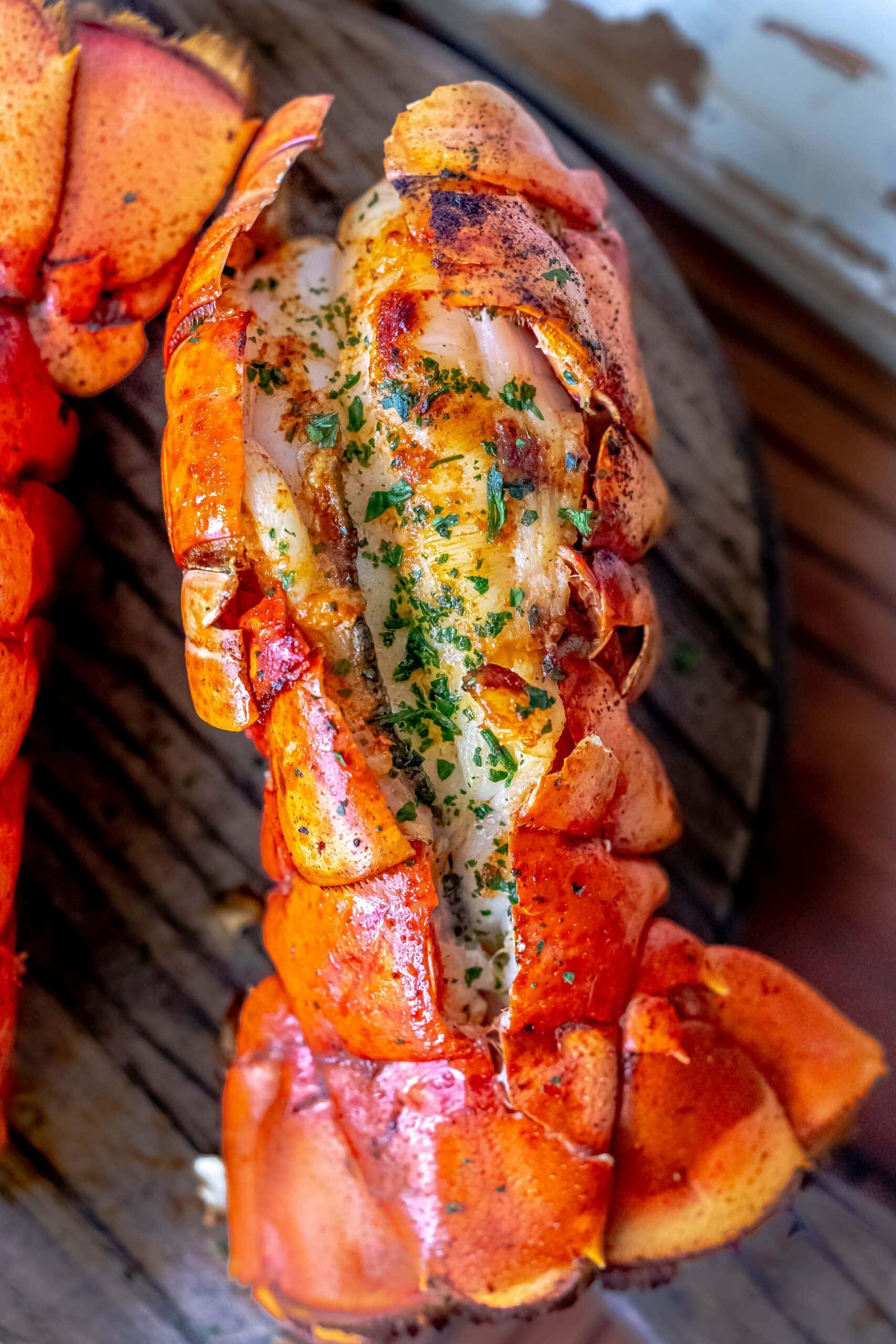 Grilled lobster tails with lemon garlic butter on a wooden plate.