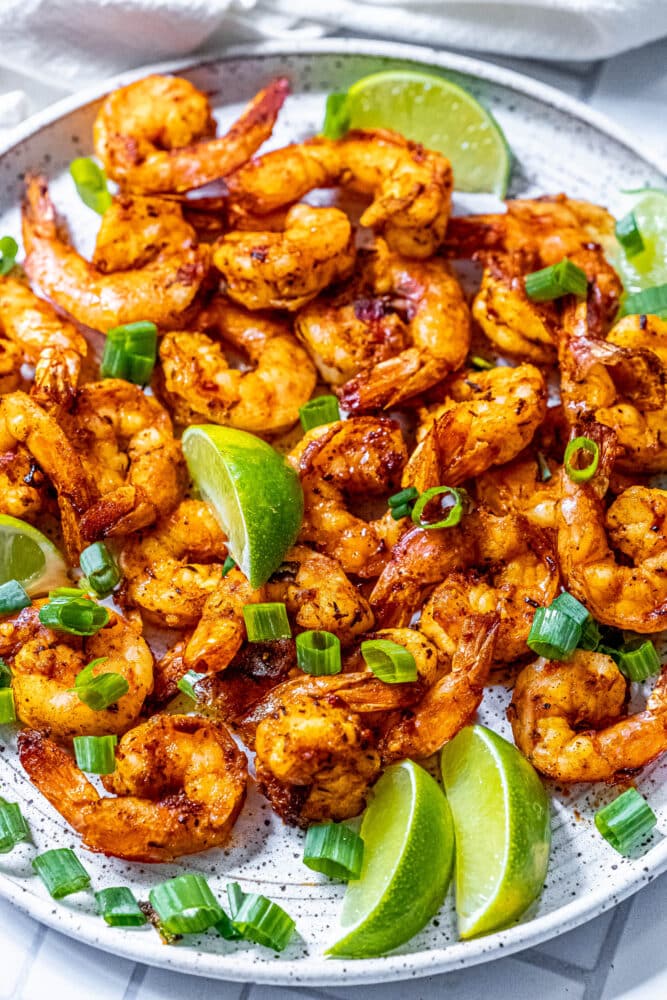 picture of jerk shrimp on a white plate with sliced green onions and limes