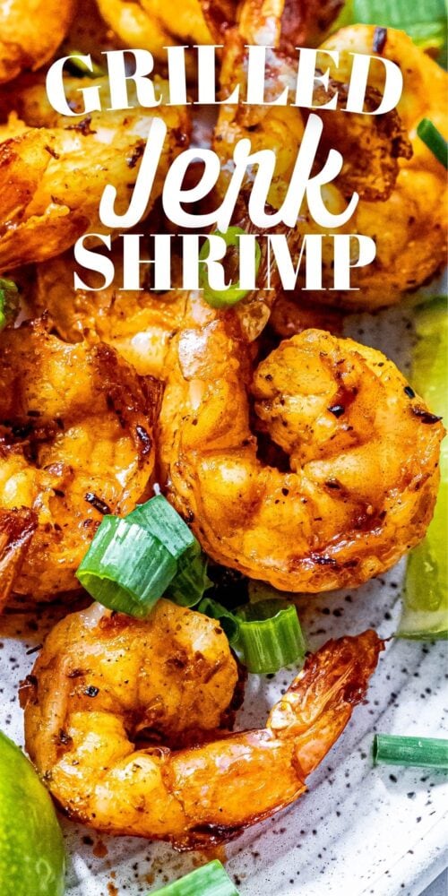 picture of jerk shrimp on a white plate with sliced green onions and limes