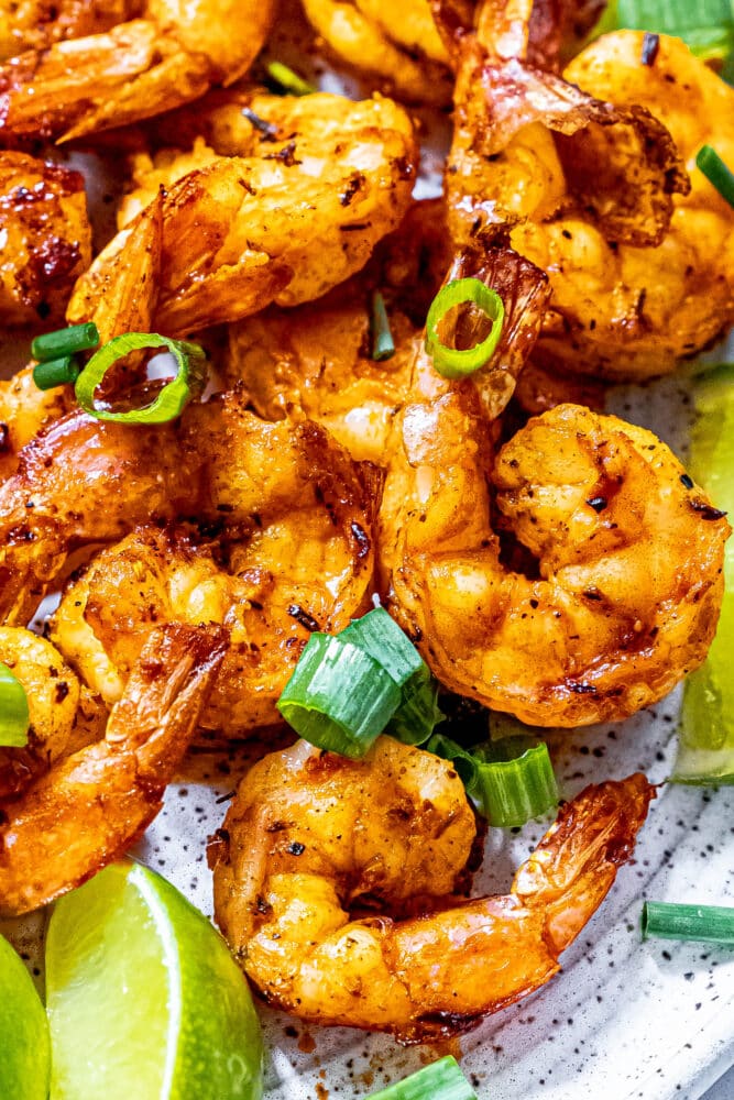 picture of jerk shrimp on a white plate with sliced green onions and limes