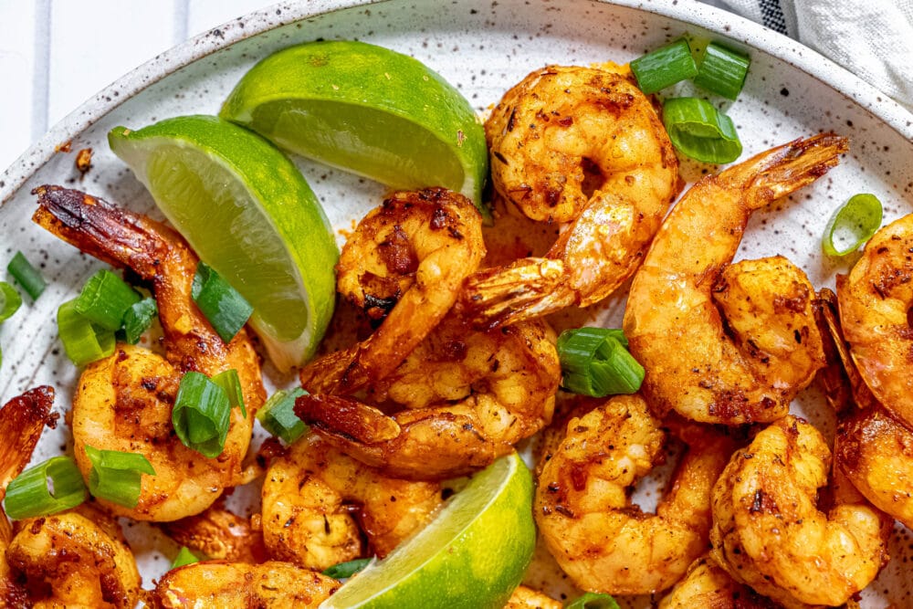 picture of jerk shrimp on a white plate with sliced green onions and limes