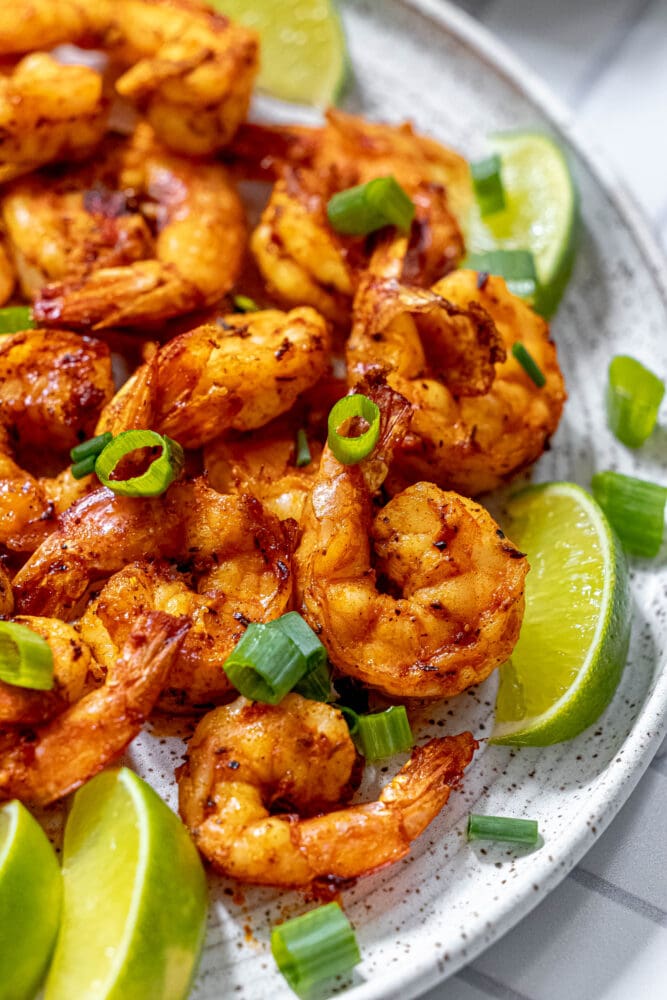 picture of jerk shrimp on a white plate with sliced green onions and limes