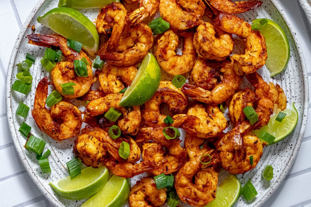 picture of jerk shrimp on a white plate with sliced green onions and limes