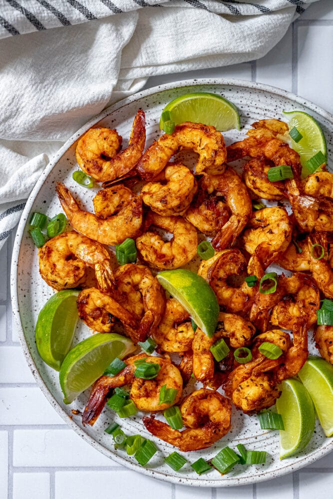 picture of jerk shrimp on a white plate with sliced green onions and limes