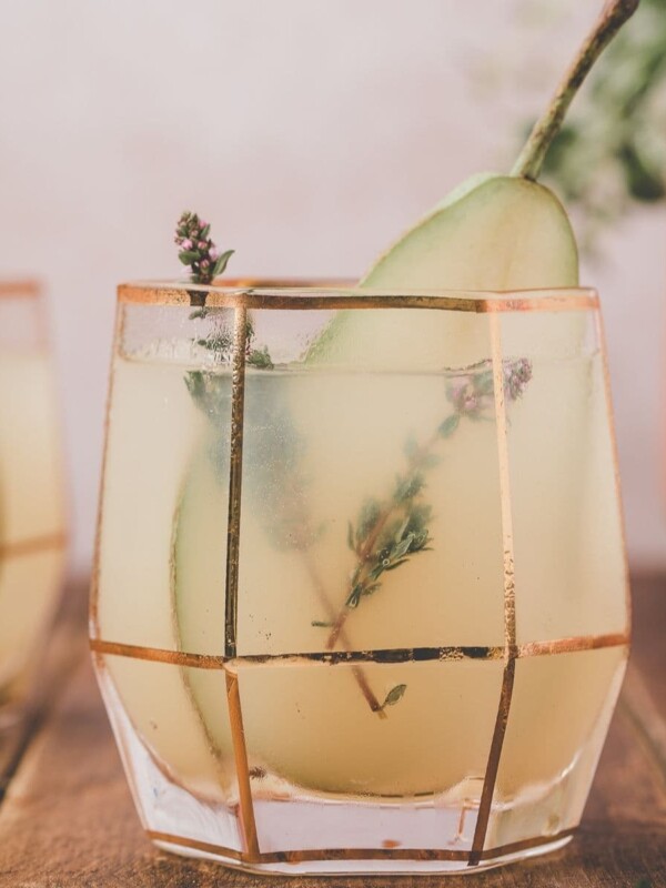 two cocktails with a slice of pear and herbs as a garnish