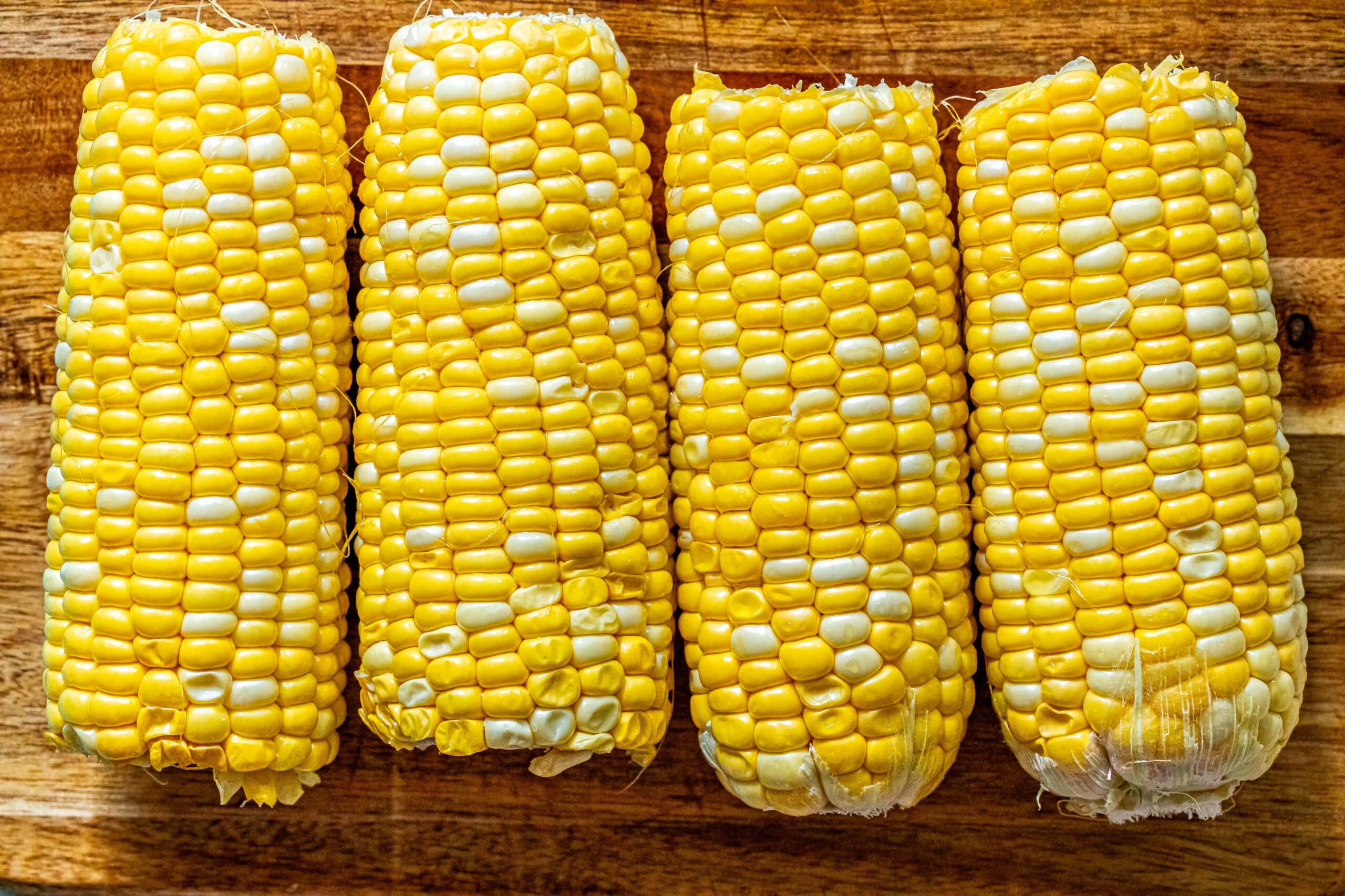 The best grilled corn on the cob recipe displayed with four ears of corn sitting on a wooden cutting board.