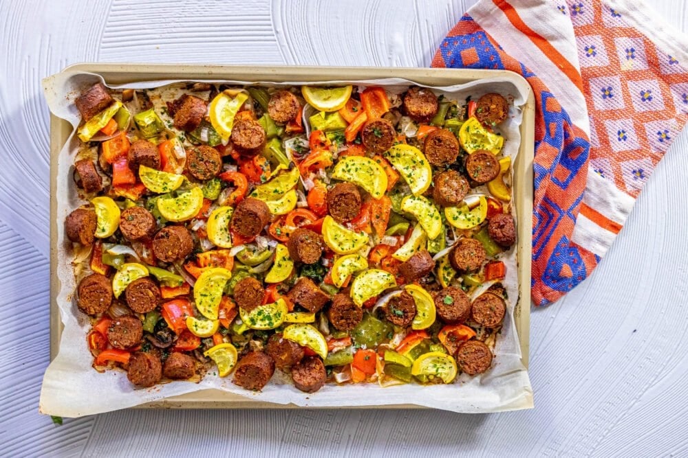 picture of baked vegan chorizo sausage, squash, peppers, onions, and mushrooms on a baking sheet