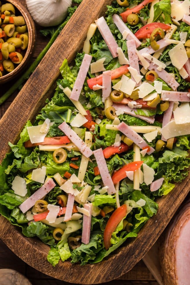 picture of julienne kale salad with meat cheese and vegetables with a Mediterranean dressing in a wood bowl on a table