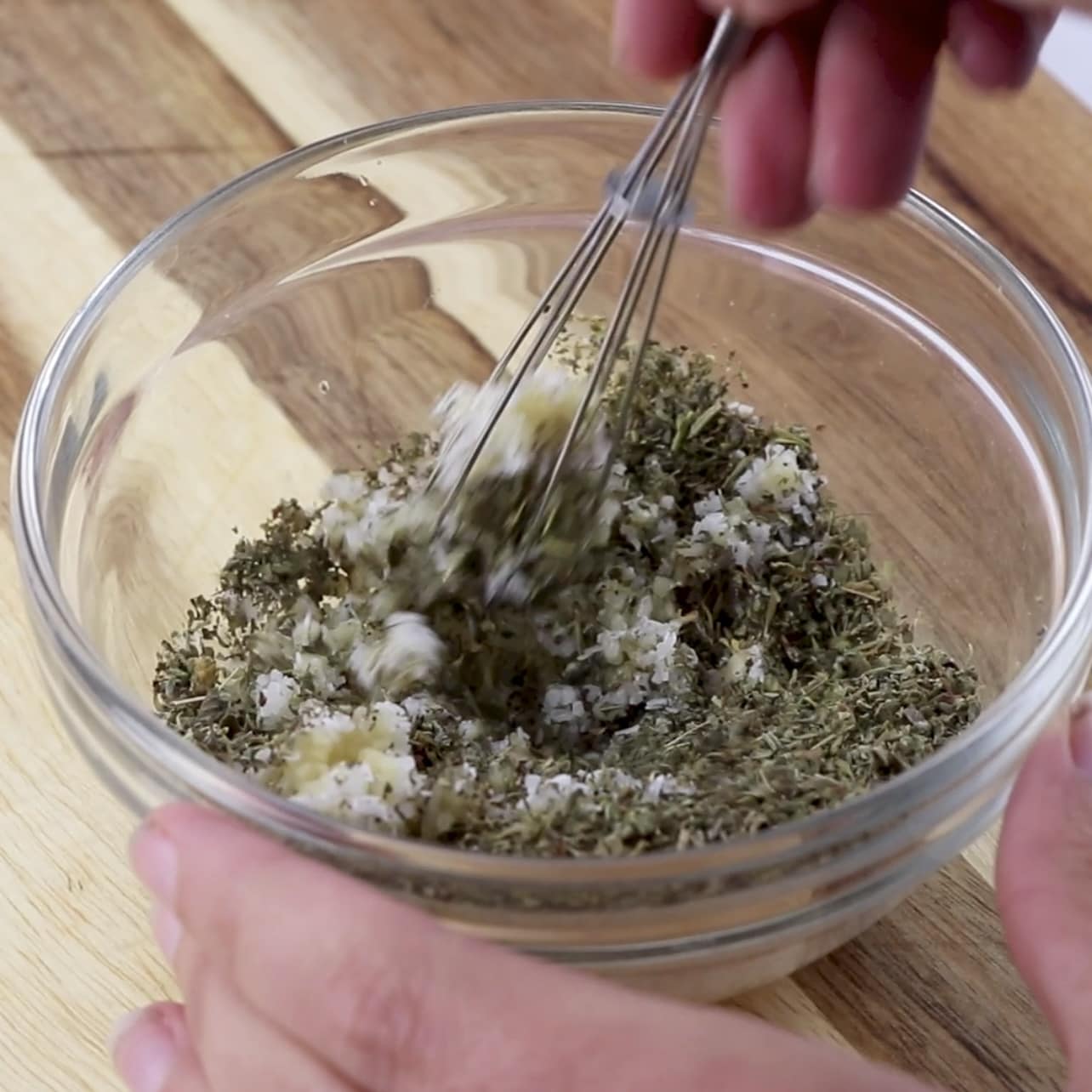 a hand mixing herbs and salt in a bowl