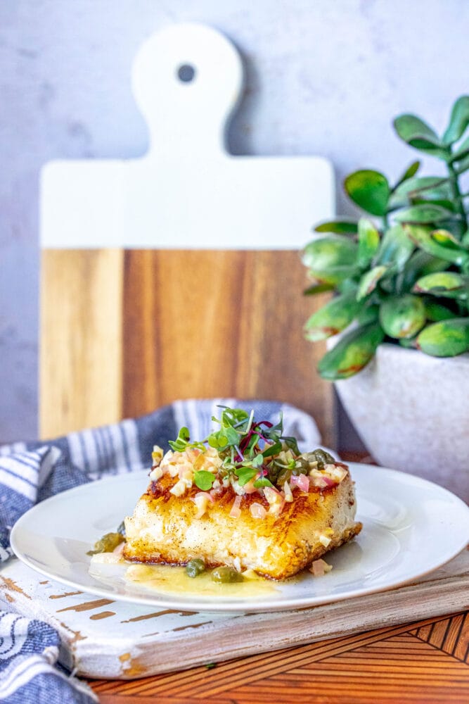 pan fried seabass with lemon caper butter sauce on top on a white plate