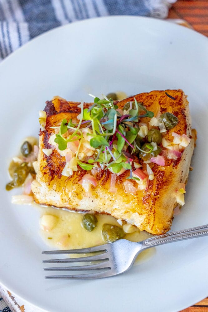 pan fried seabass with lemon caper butter sauce on top on a white plate