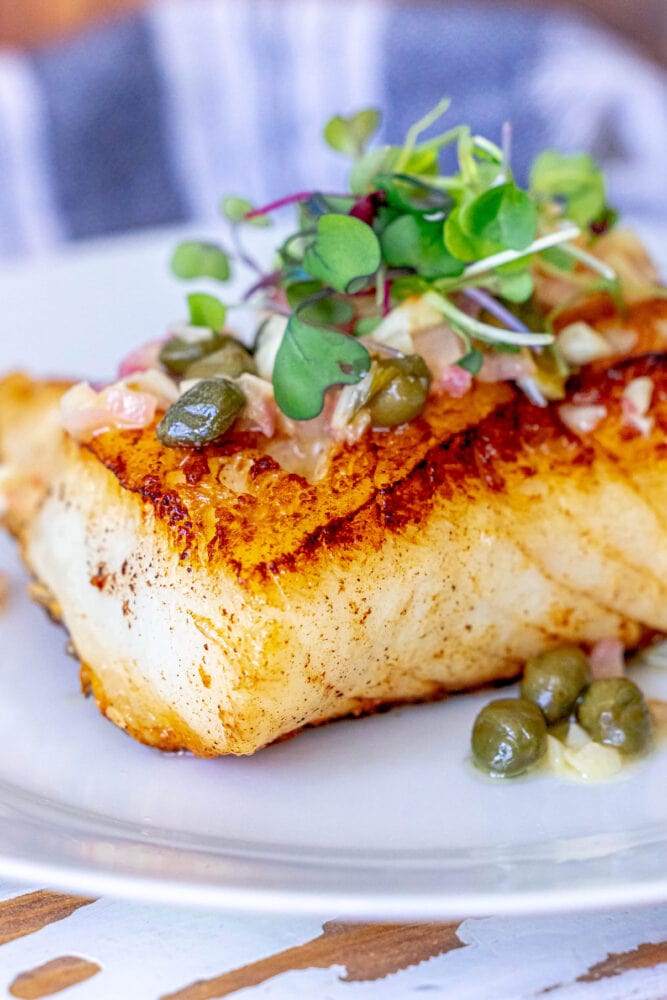 pan fried seabass with lemon caper butter sauce on top on a white plate