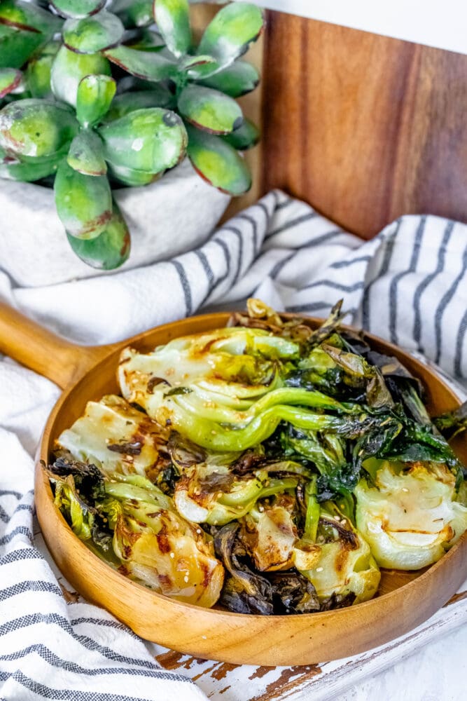 picture of grilled bok choy with sesame seeds on a wood platter on a table