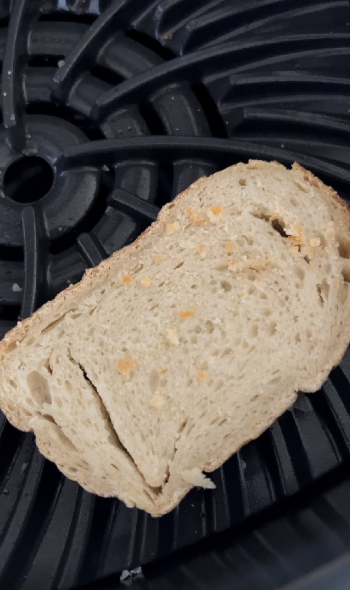 A slice of bread with some crumbs sits on a black tray with a circular, grooved pattern, evoking the rustic charm of a french goat cheese salad.