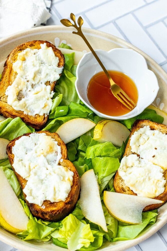 picture of butter lettuce salad in a bowl topped with bread with goat cheese, honey, pears, and champagne vinaigrette dressing