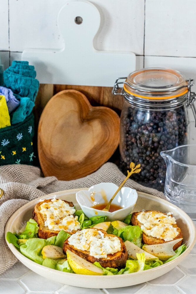 picture of butter lettuce salad in a bowl topped with bread with goat cheese, honey, pears, and champagne vinaigrette dressing