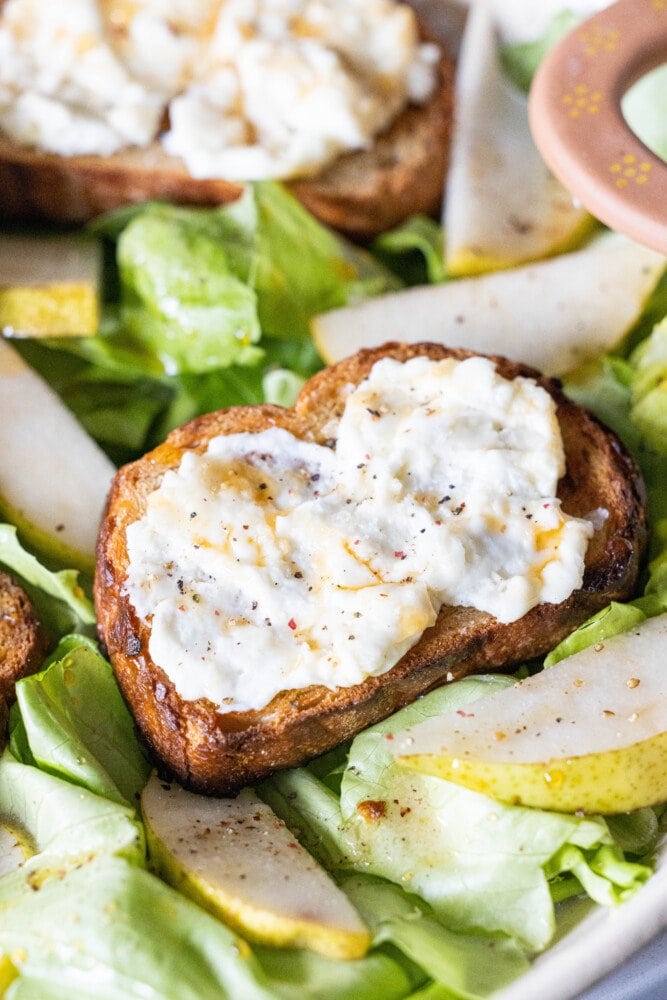 picture of butter lettuce salad in a bowl topped with bread with goat cheese, honey, pears, and champagne vinaigrette dressing