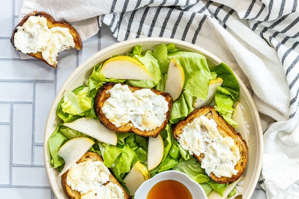 picture of butter lettuce salad in a bowl topped with bread with goat cheese, honey, pears, and champagne vinaigrette dressing