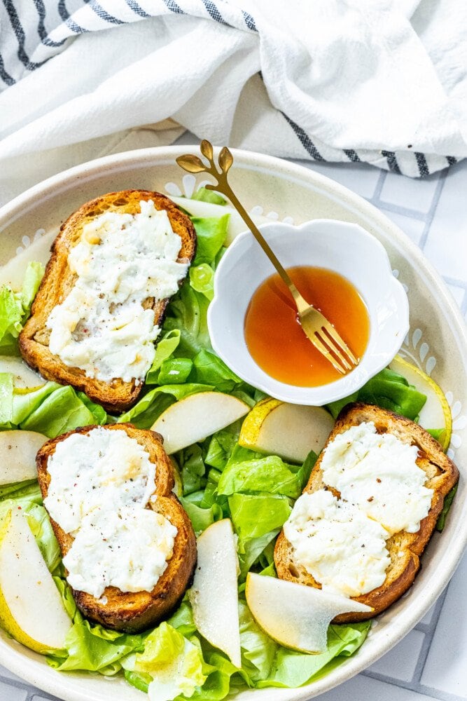 picture of butter lettuce salad in a bowl topped with bread with goat cheese, honey, pears, and champagne vinaigrette dressing