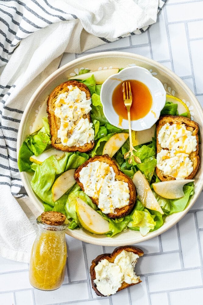 picture of butter lettuce salad in a bowl topped with bread with goat cheese, honey, pears, and champagne vinaigrette dressing