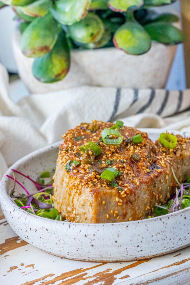 picture of tuna steak on a white plate topped with sesame seeds and green onions