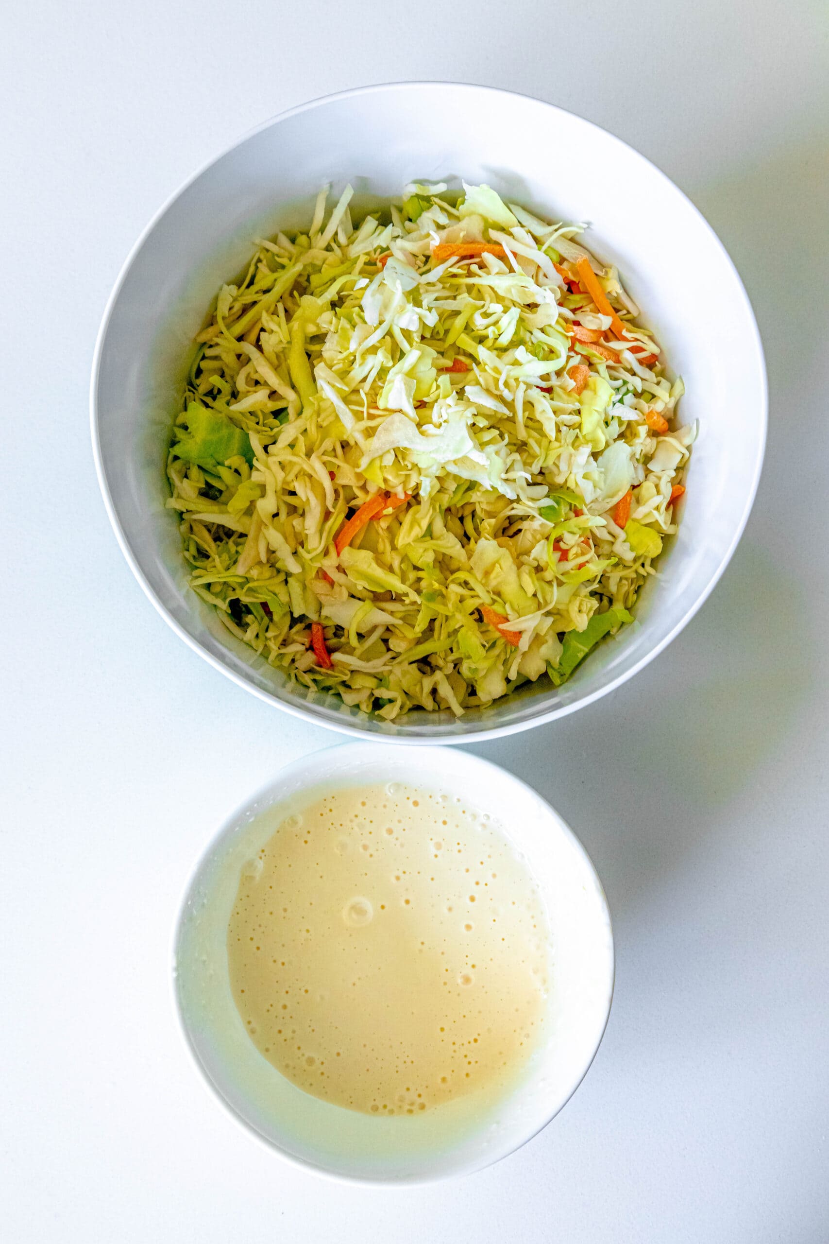 picture of coleslaw dressing in a small bowl next to a bowl of shredded cabbage and carrots
